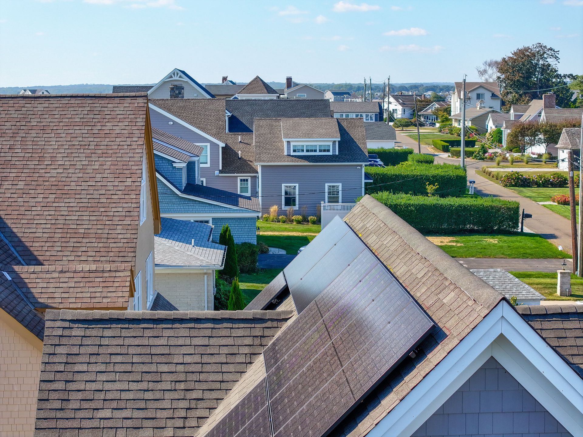 Rooftops of suburban houses with gray shingles and blue walls under a clear sky