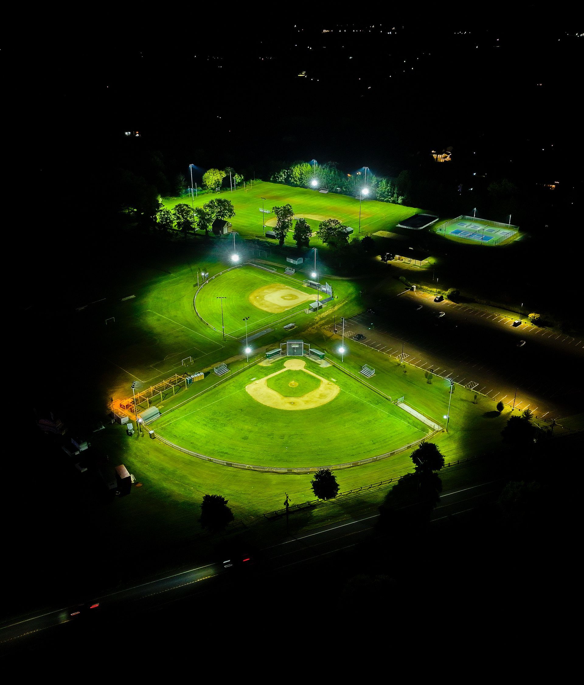 Aerial night view of a brightly lit sports field and surrounding green park with scattered lights