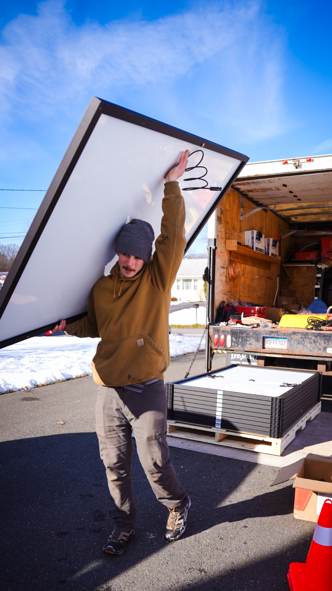 Person carrying a large white panel outdoors beside a truck in a snowy work area