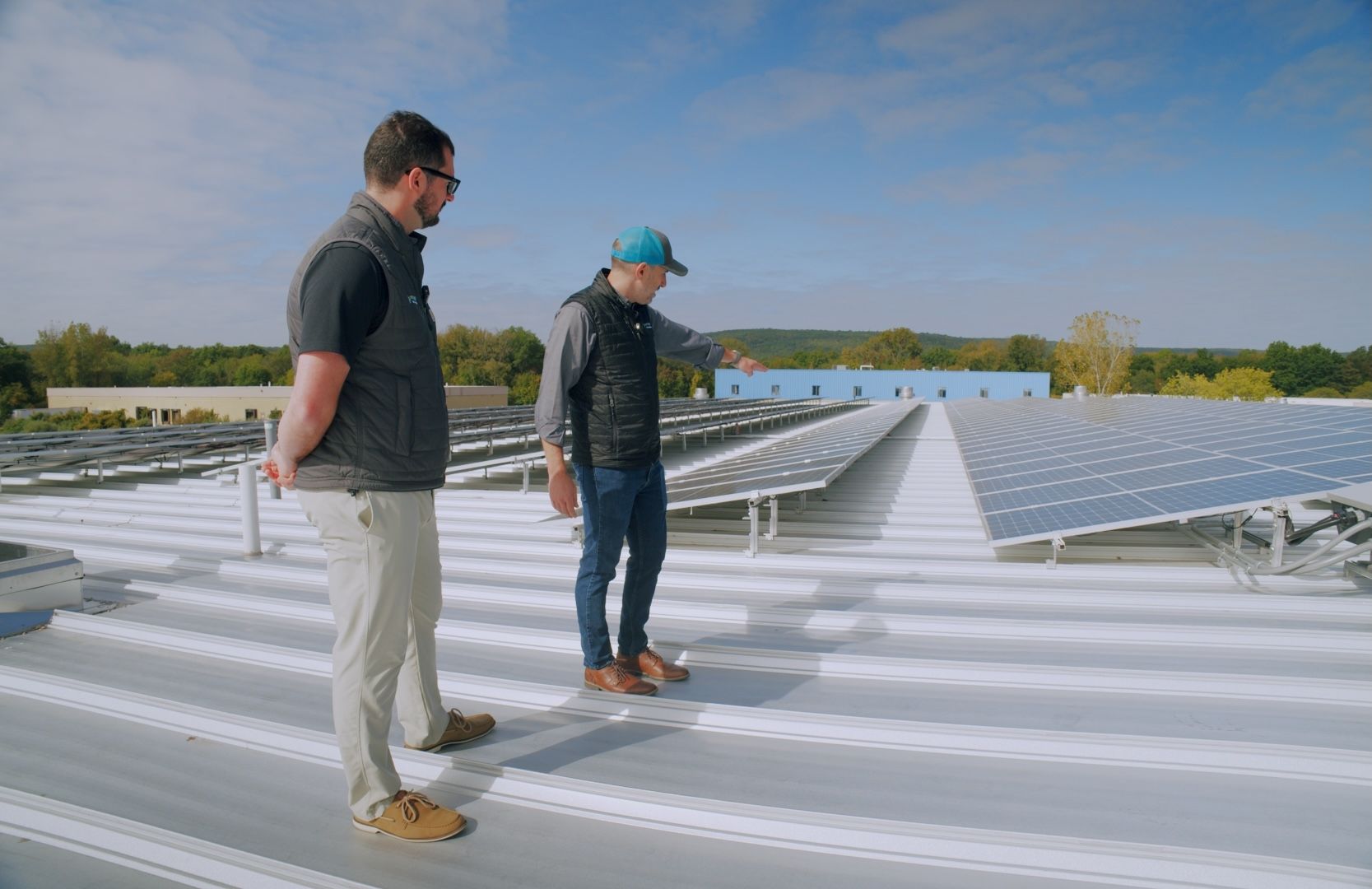 Two people inspecting solar panels on a rooftop under a blue sky