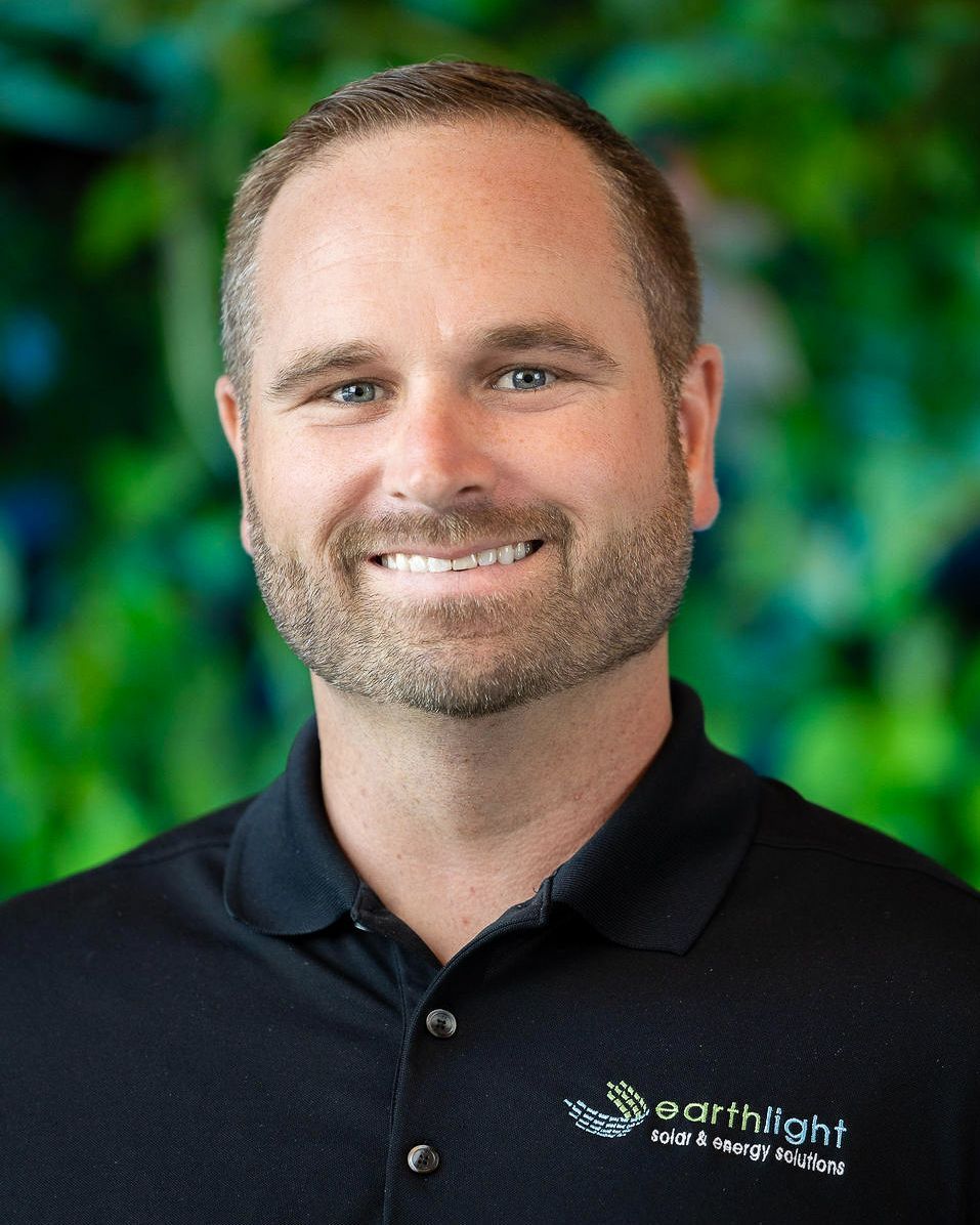 Smiling man in a black polo shirt with a logo, standing before a green blurred background.