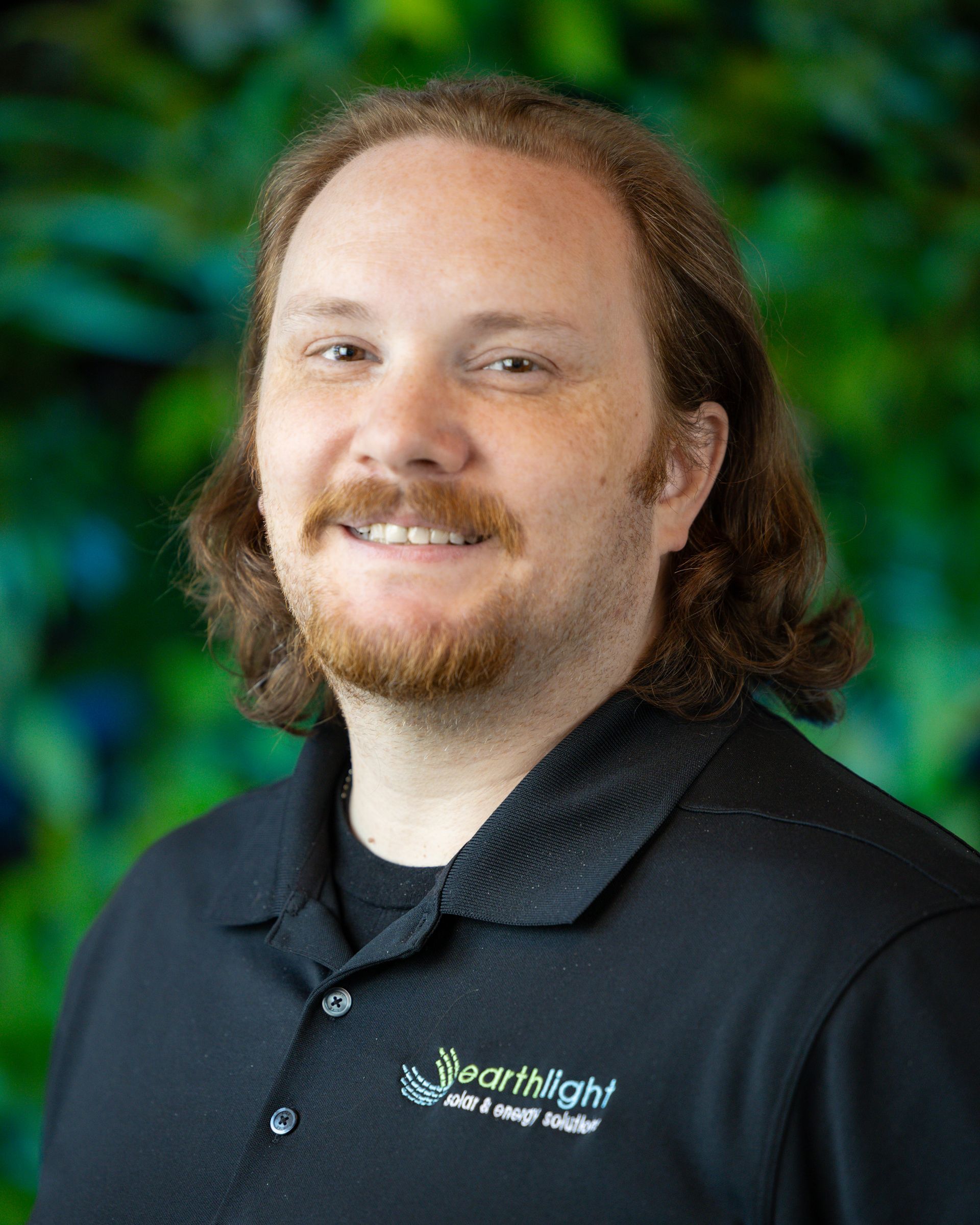 Smiling person in a black polo shirt before a green, blurred background
