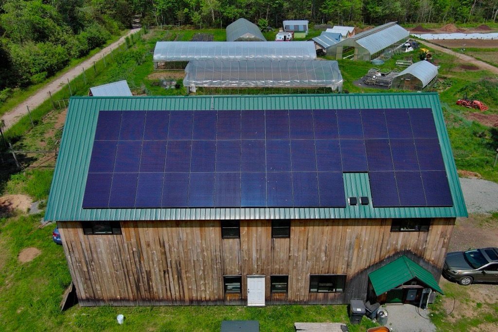 Aerial view of a wooden building with a large solar panel roof in a rural area