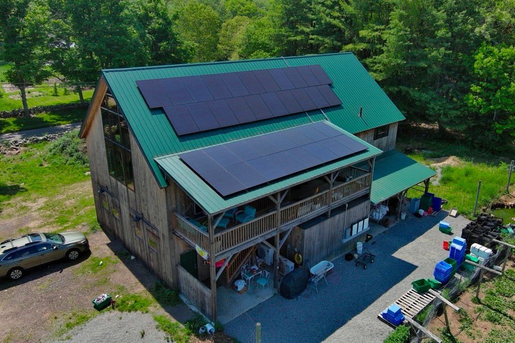 Rural house with green roof and solar panels, surrounded by trees and farm equipment.