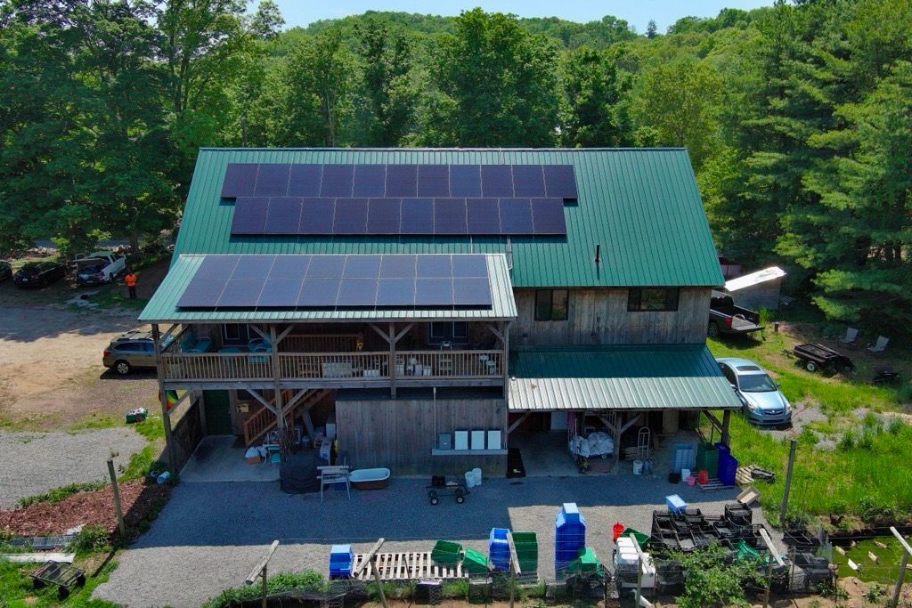 Rural house with green roof and solar panels, surrounded by trees and a garden