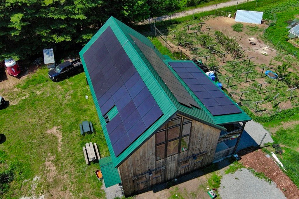 Aerial view of a small building with a green roof and dark solar panels beside a grassy path