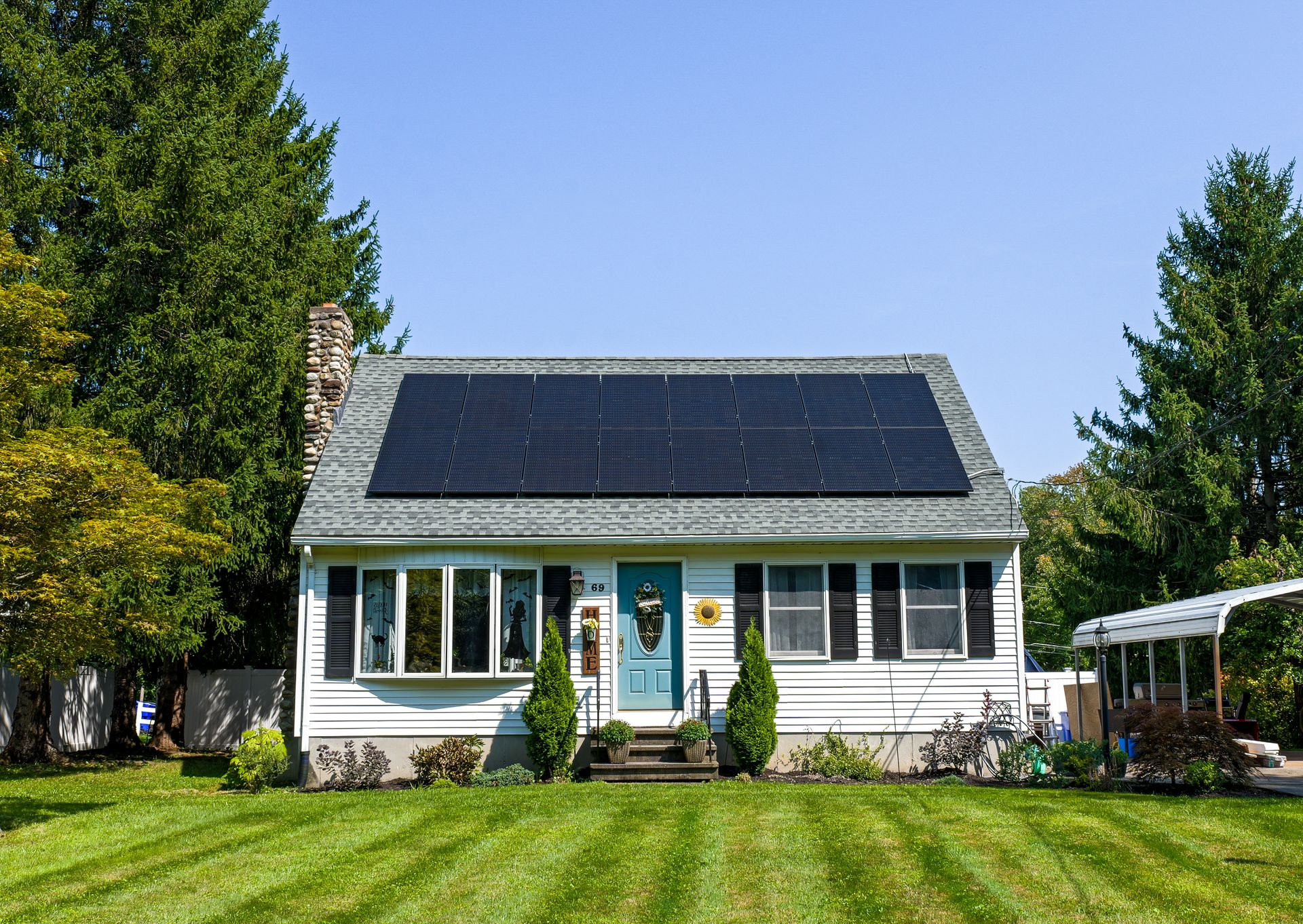 White house with a solar-panel roof, front porch, and green lawn under a clear blue sky.