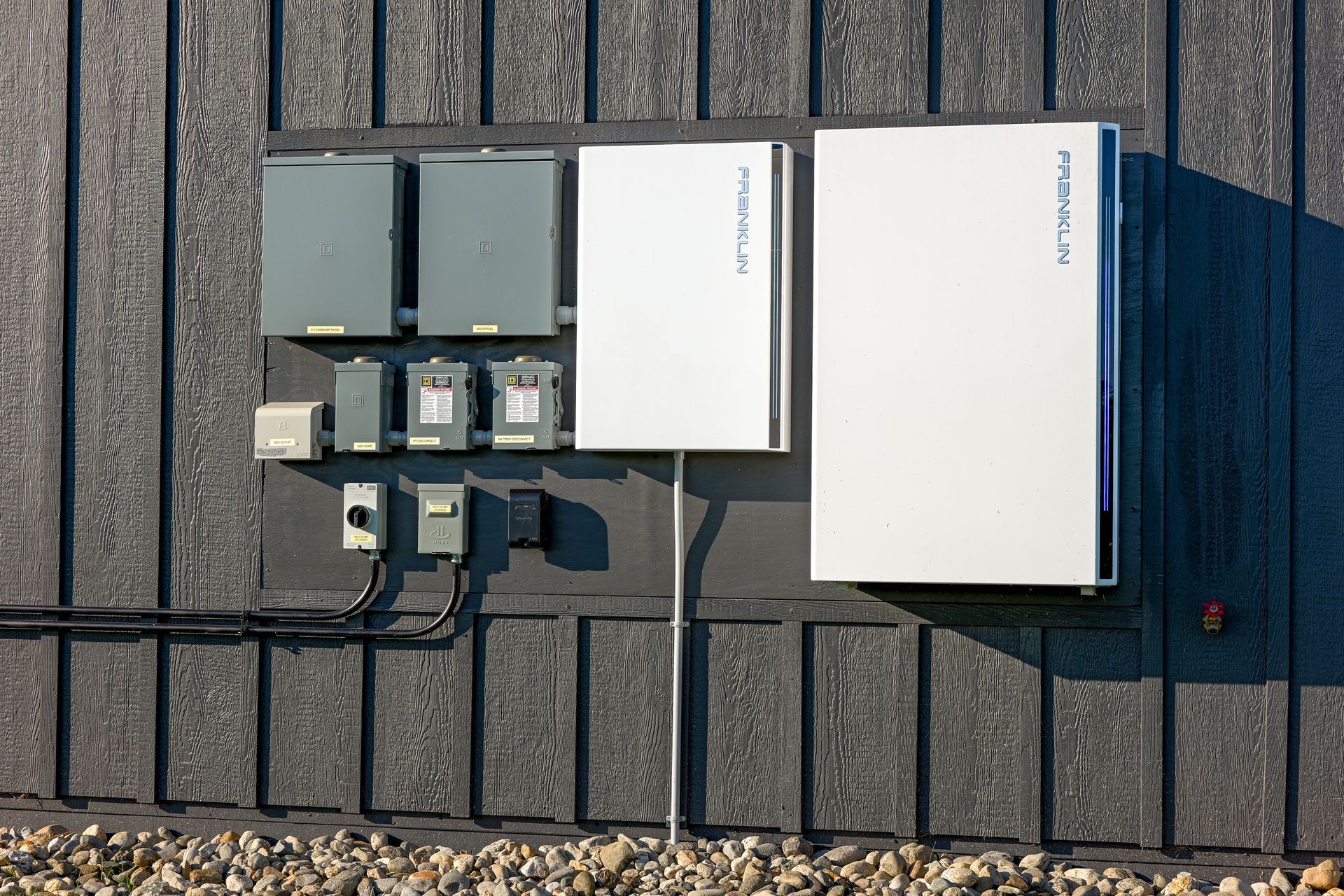 Outdoor electrical equipment mounted on a gray wall with solar panels and wiring