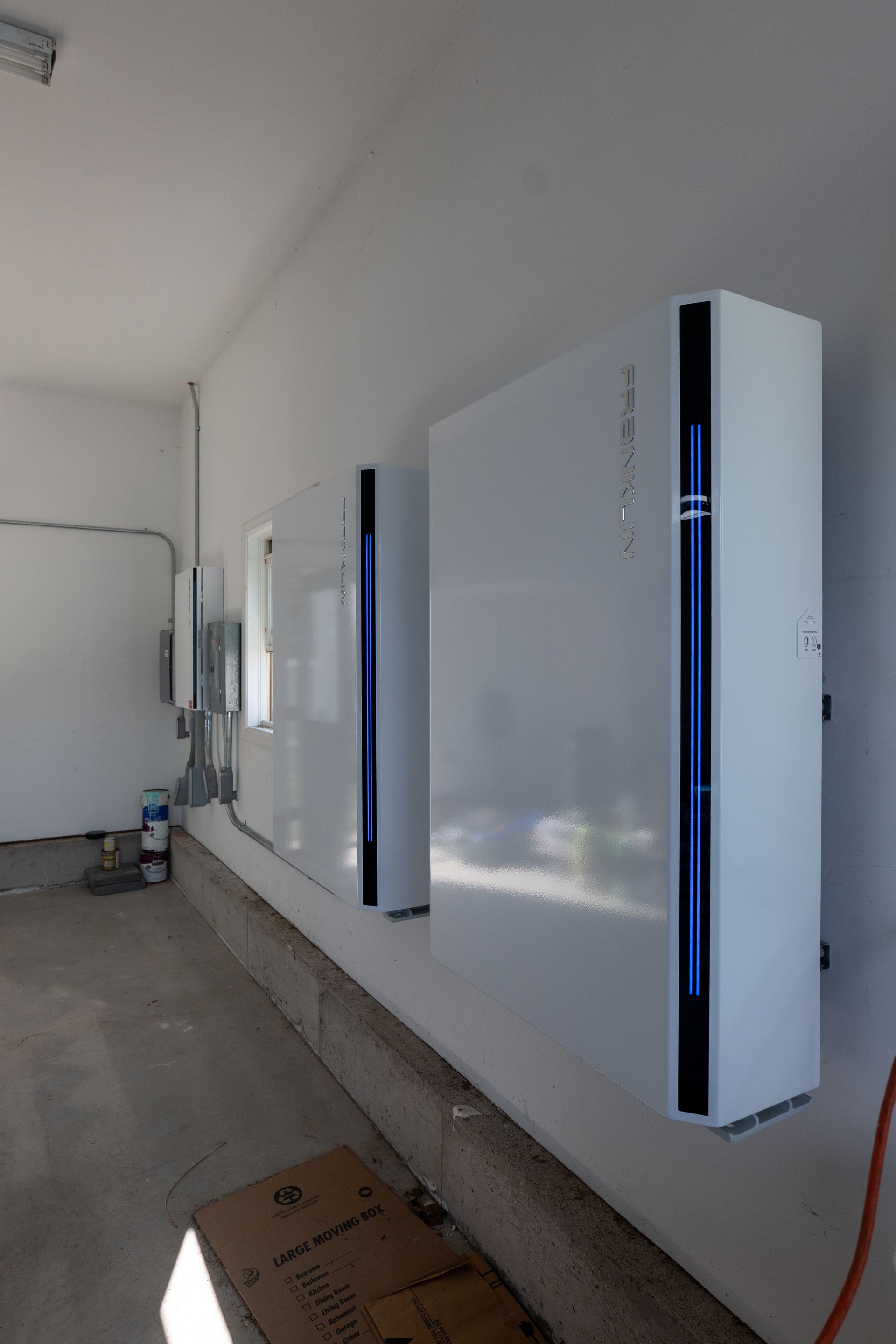 Row of wall-mounted white appliances with blue vertical lights in a bare indoor hallway
