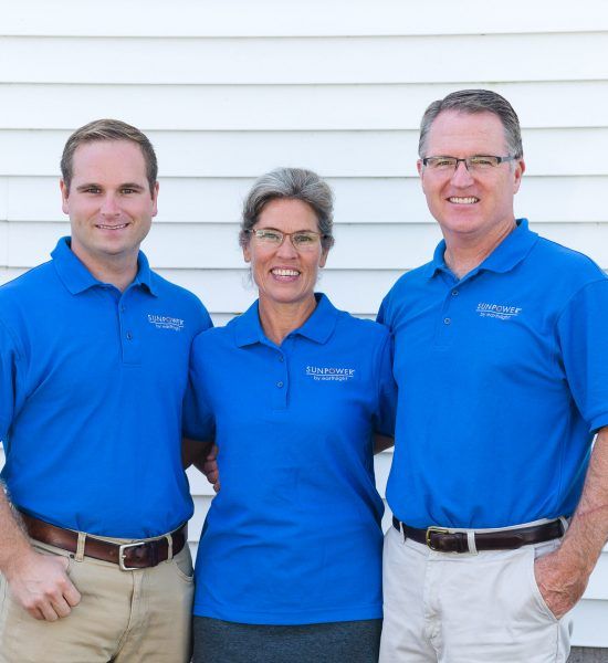 Three people in blue polo shirts standing together in front of white siding
