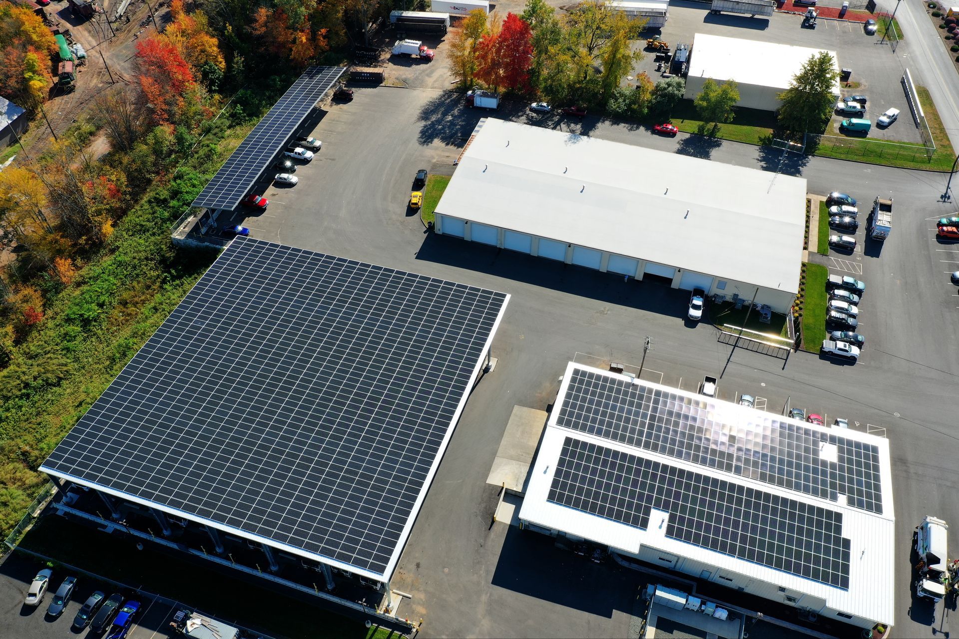 Aerial view of an industrial site with solar-paneled roofs, parked cars, and trees