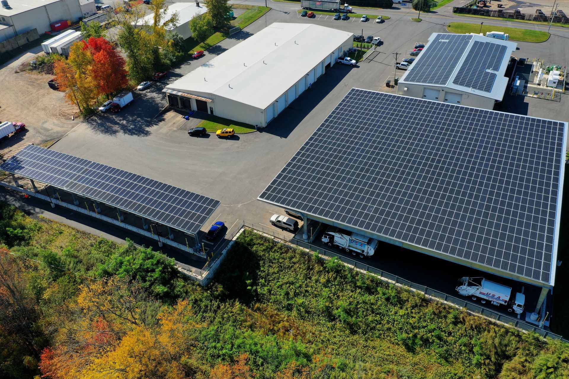 Aerial view of a solar-powered industrial site with large rooftops covered in solar panels and autumn trees nearby