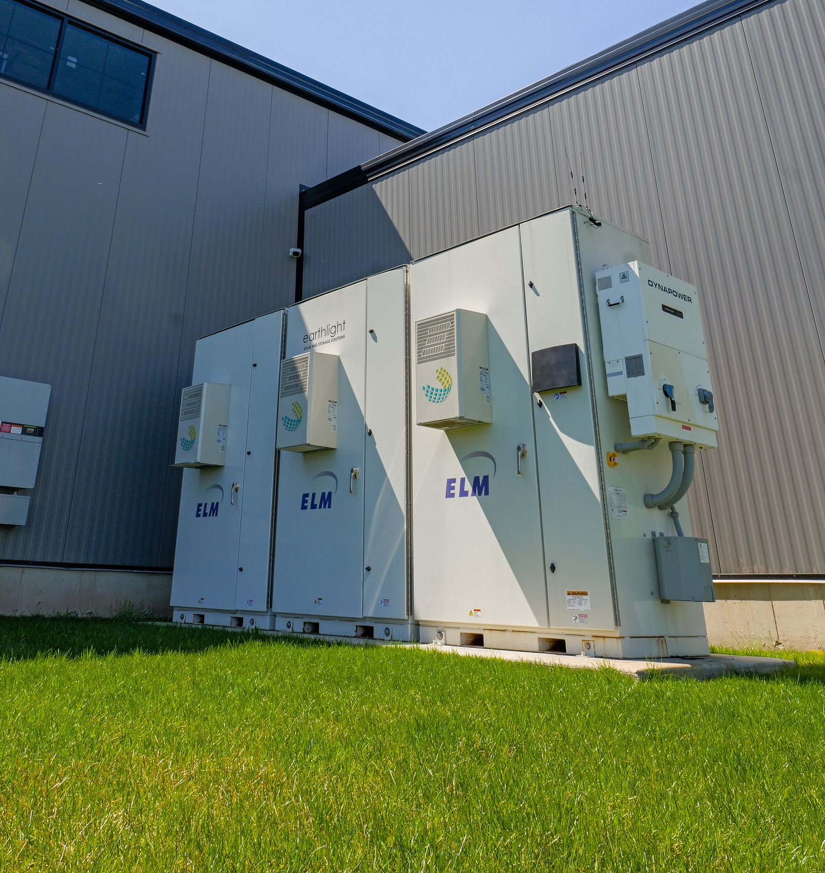Outdoor electrical equipment units beside a gray industrial building under a blue sky