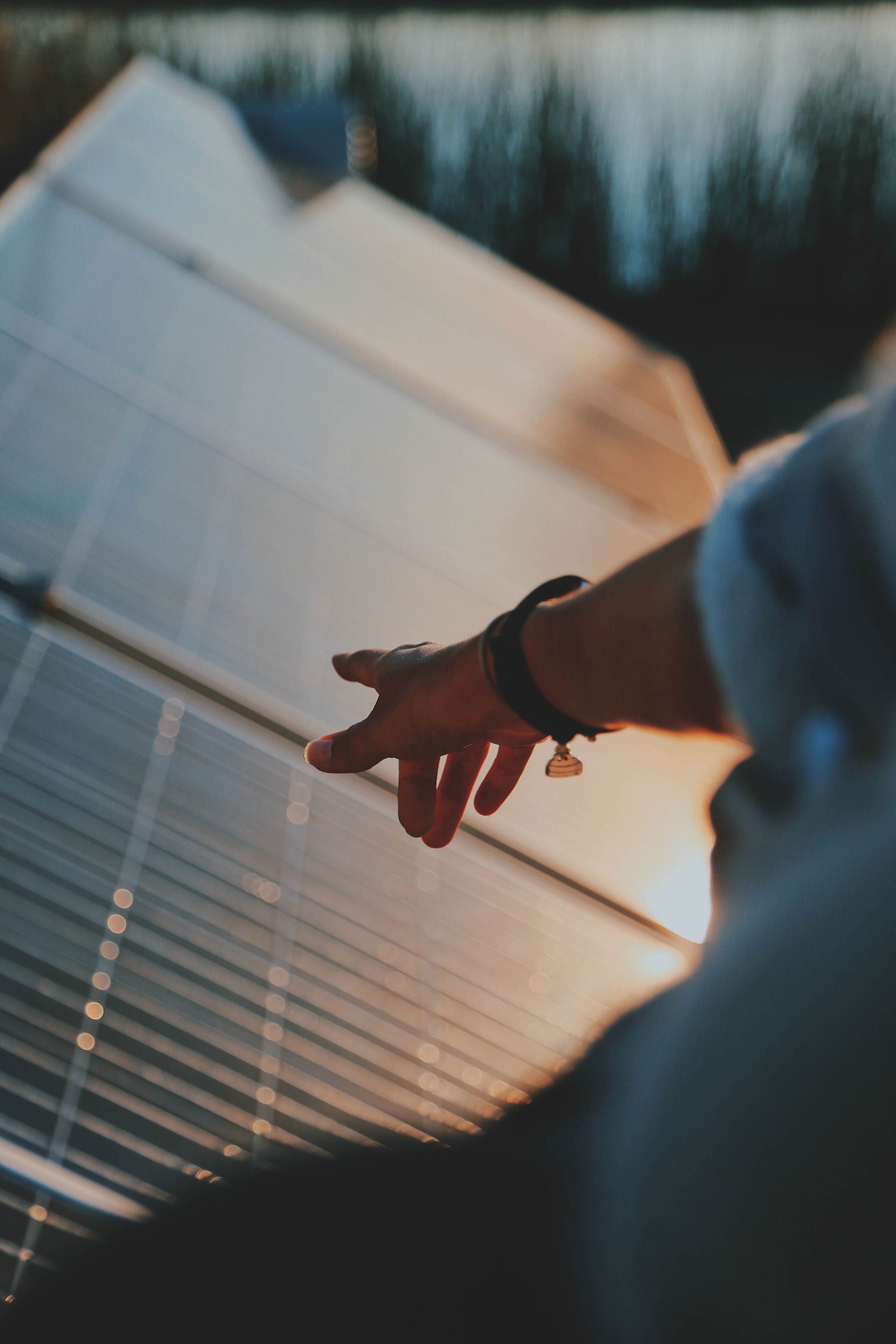 Hand pointing at solar panels in warm sunlight, with trees blurred in the background