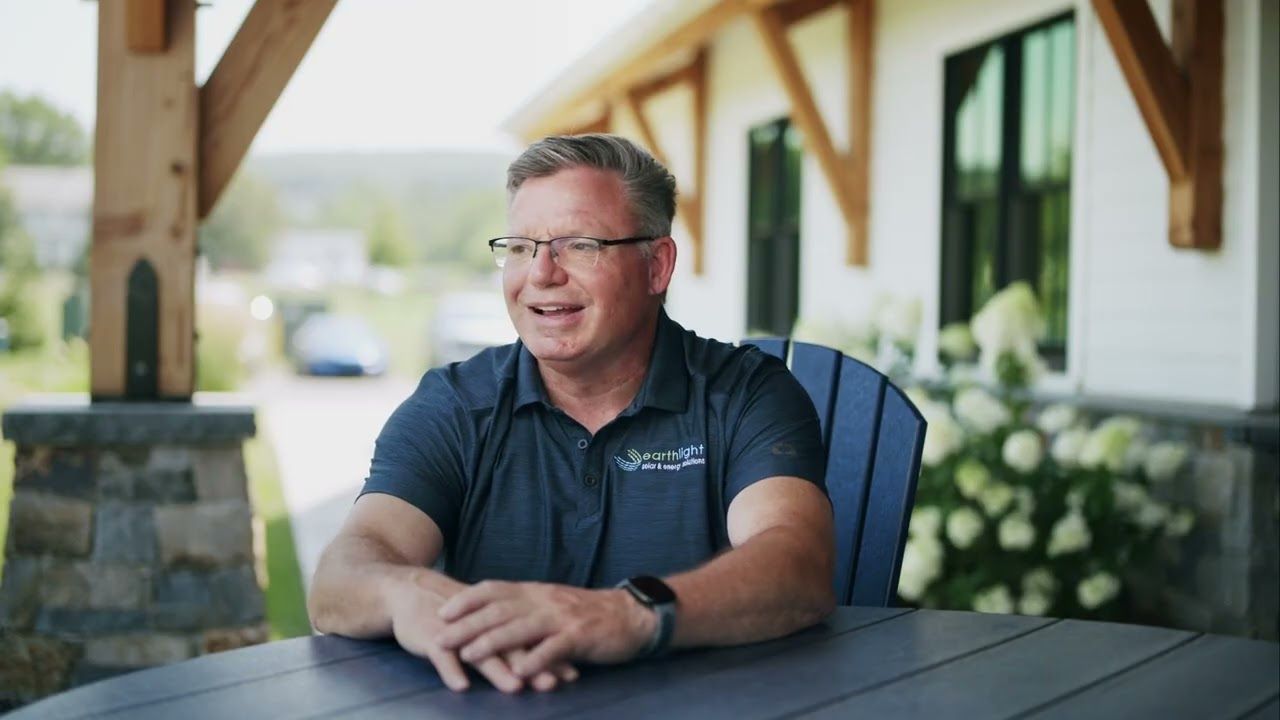 Man sitting at an outdoor picnic table, smiling in a covered patio area.