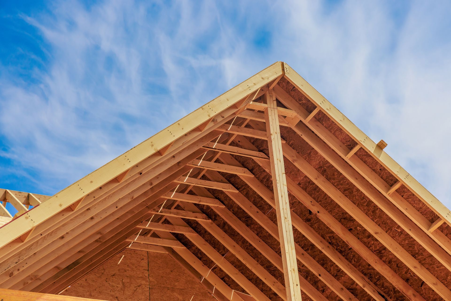 Wooden roof trusses against a blue sky with wispy clouds