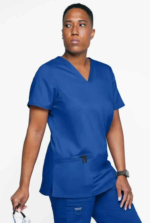 Person wearing blue scrubs, looking to the side, holding eyeglasses.