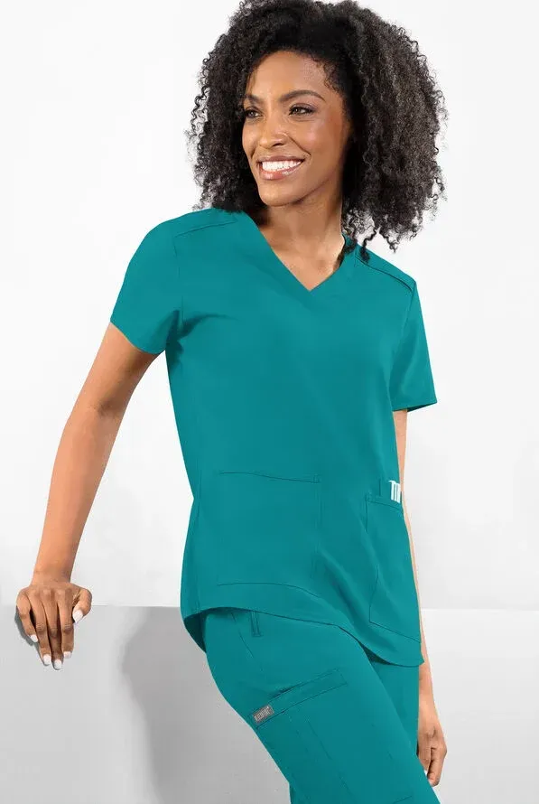 Woman in teal scrubs smiles, leaning against a white surface.