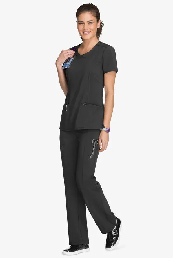 Woman in dark gray scrubs, smiling, holding a pen. Standing, indoors.
