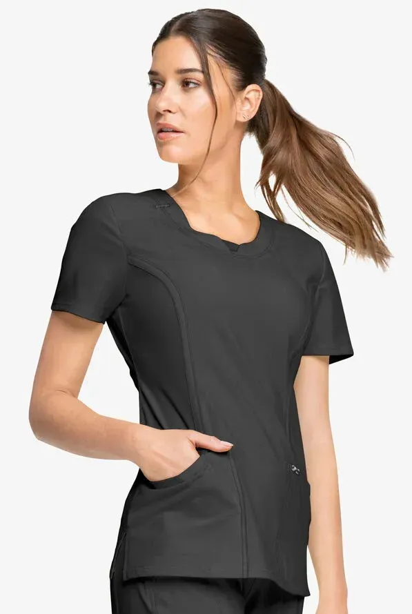 Woman in black scrub top with scalloped neckline and pocket, looking to the side.