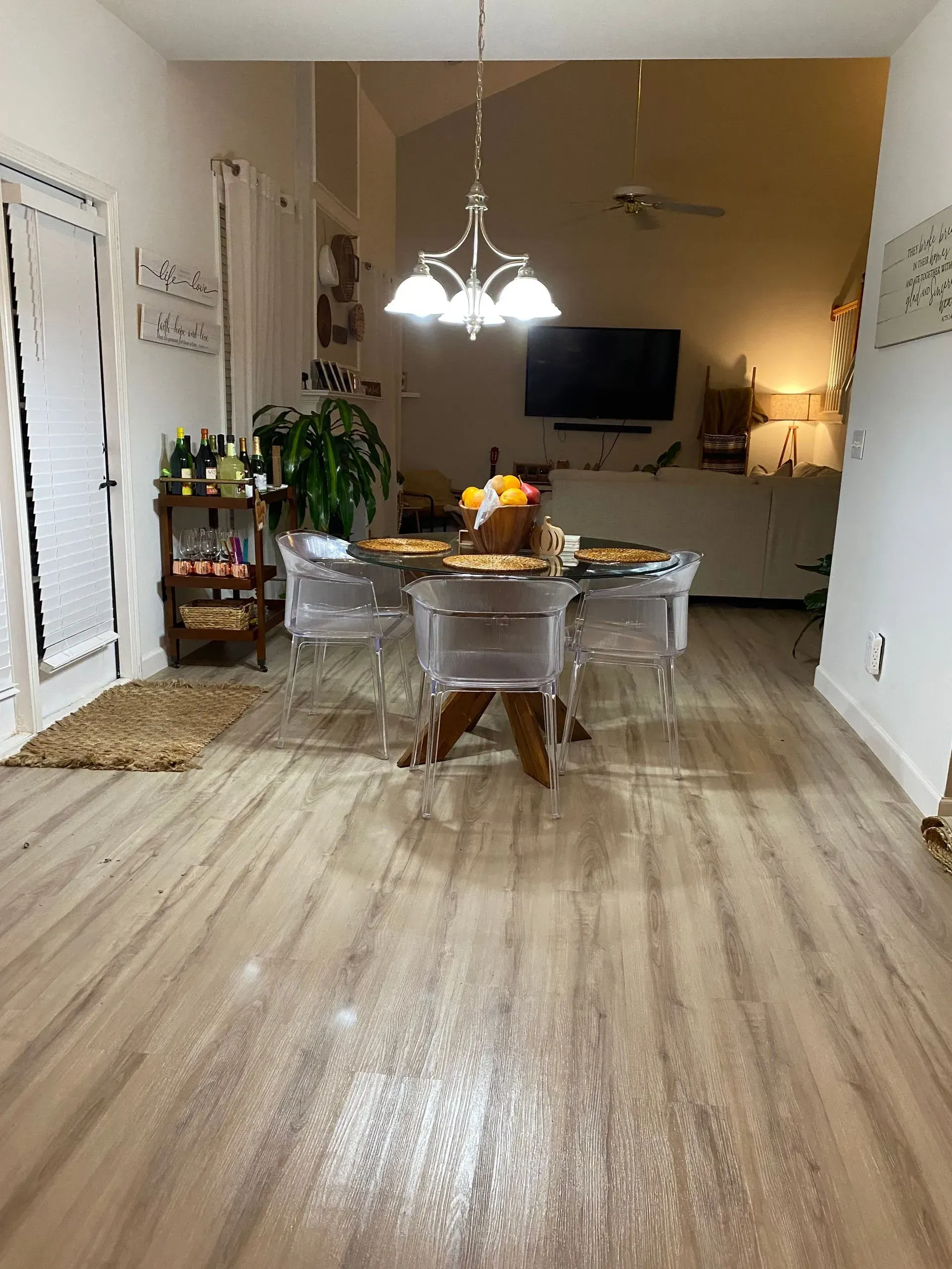 Dining room with clear chairs, round table, wooden floors, and a lit chandelier.