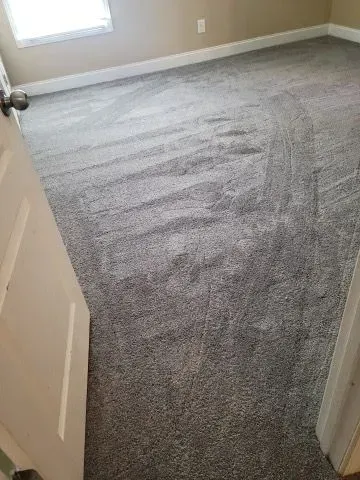 A bedroom with a gray carpeted floor and a door.