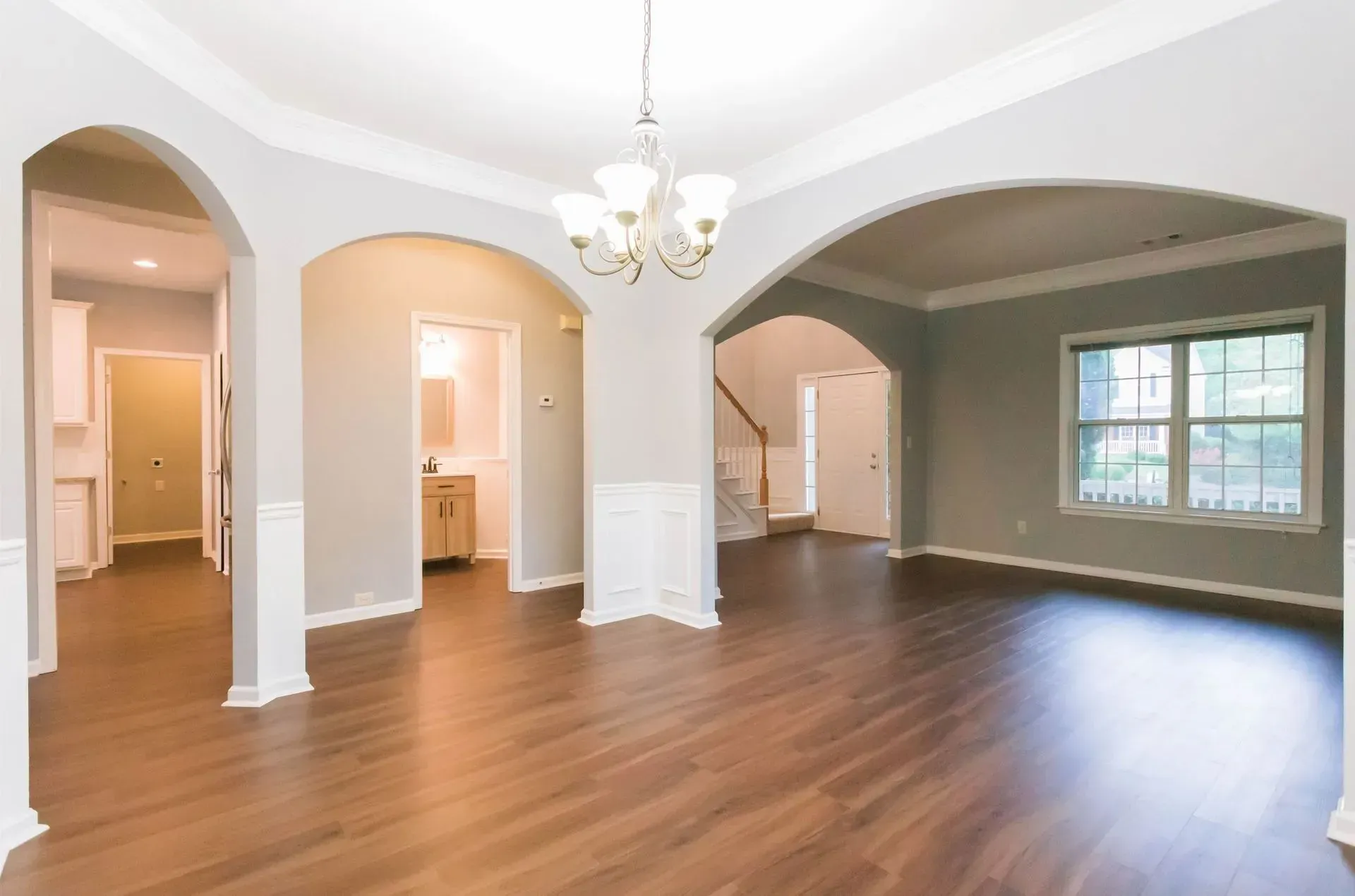 Open-concept dining room with hardwood floors, archways, and a chandelier. Light gray walls and white trim.