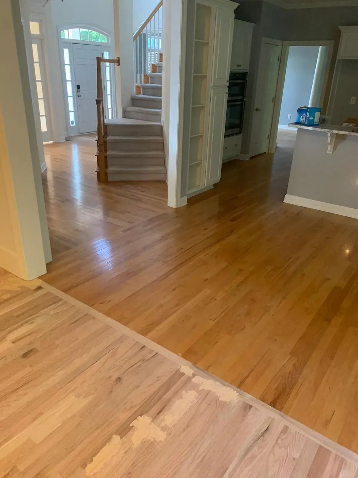 Bright hardwood foyer with staircase, white trim, and open doorway to kitchen area
