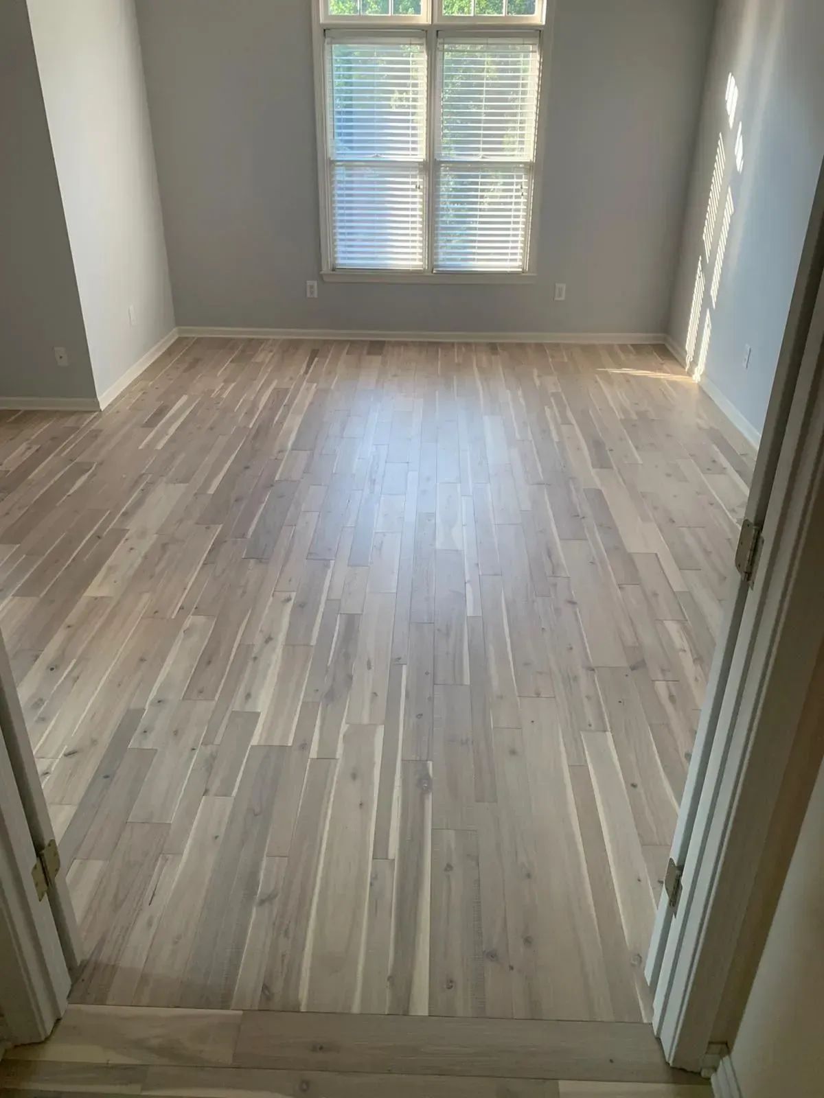 Empty room with light wood flooring, gray walls, and a window at the far end.