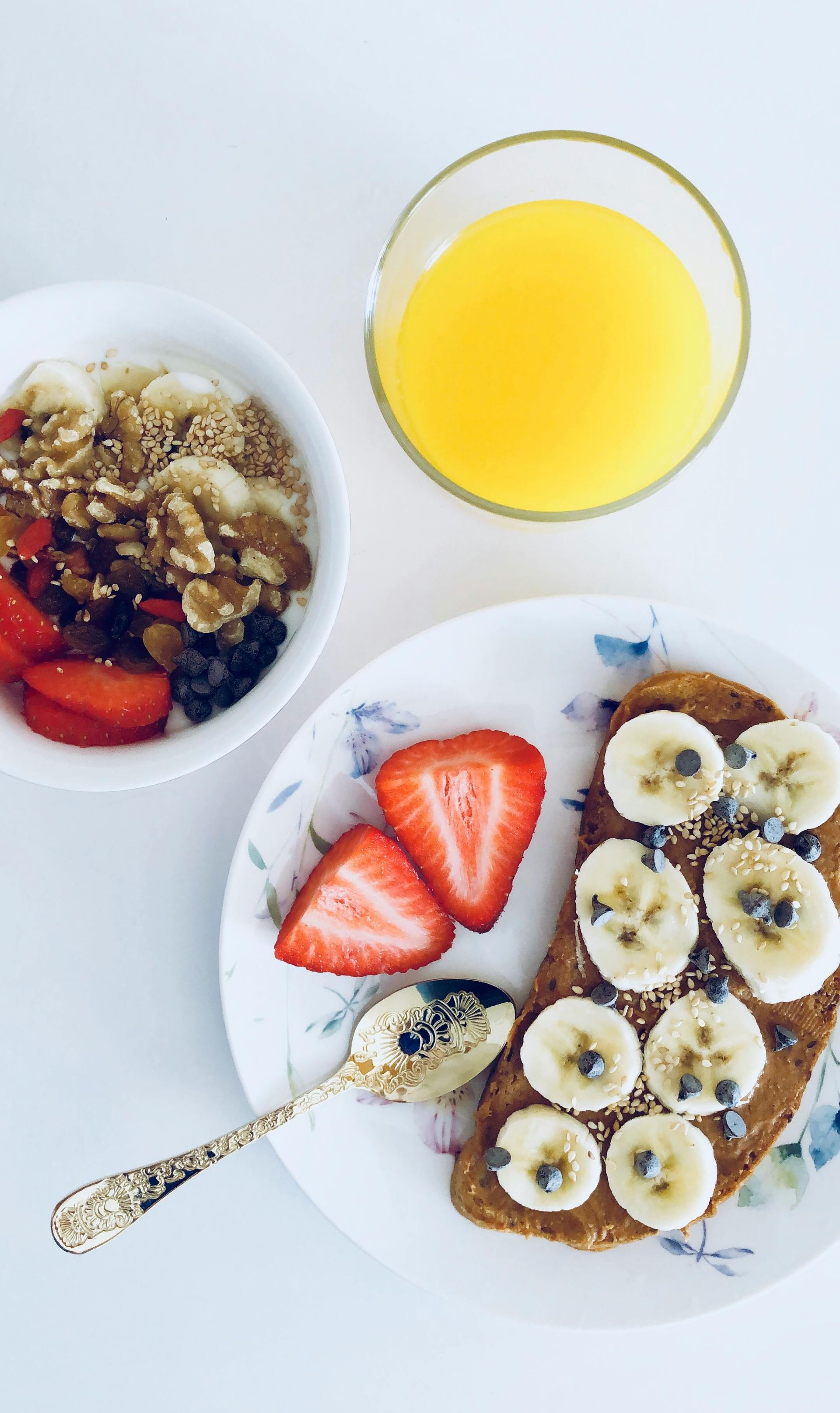 A plate of toast with bananas and strawberries next to a bowl of granola and a glass of orange juice.