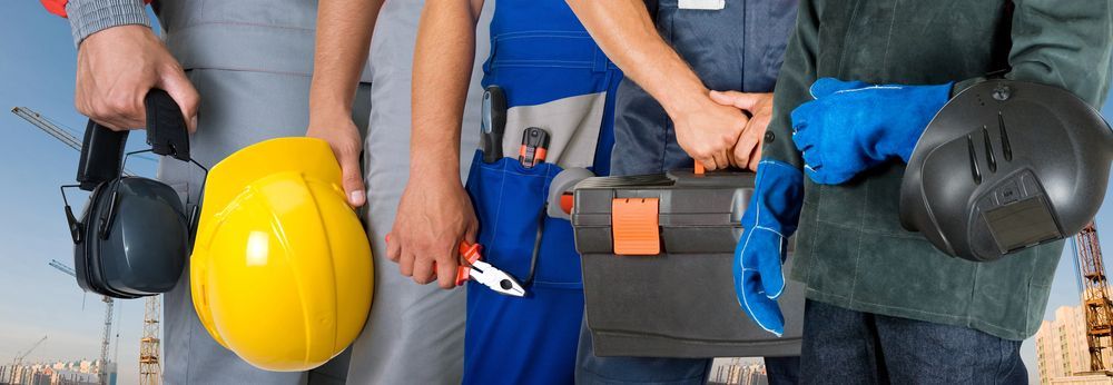 Operai che tengono in mano attrezzi e dispositivi di sicurezza in un cantiere edile.