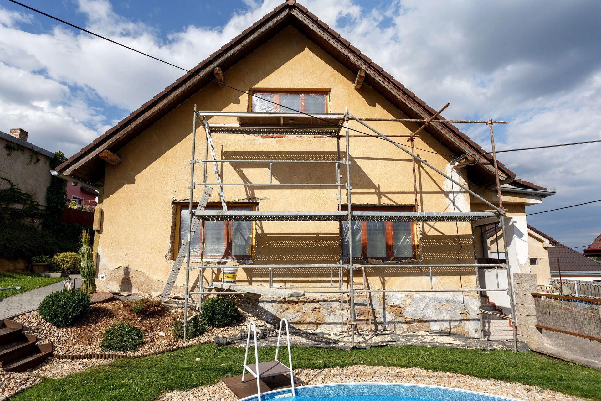 Esterno di una casa in costruzione, impalcature contro il muro, stucco giallo, cielo azzurro.