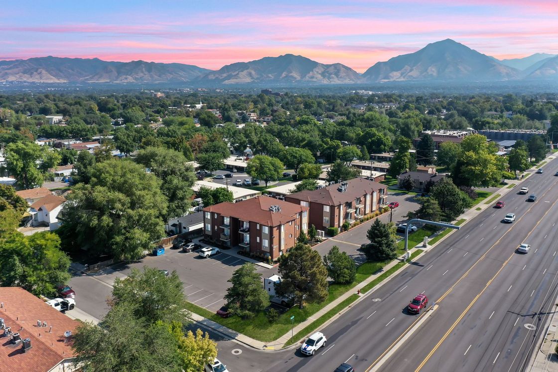 Aerial view of a suburban neighborhood with apartment buildings, a busy road, and mountains in the background at sunset.