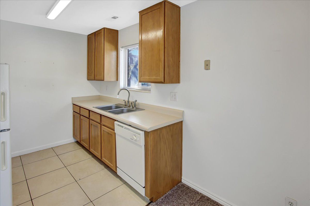 Kitchen with light cabinets, off-white countertops, a stainless steel sink, and white appliances against gray walls.