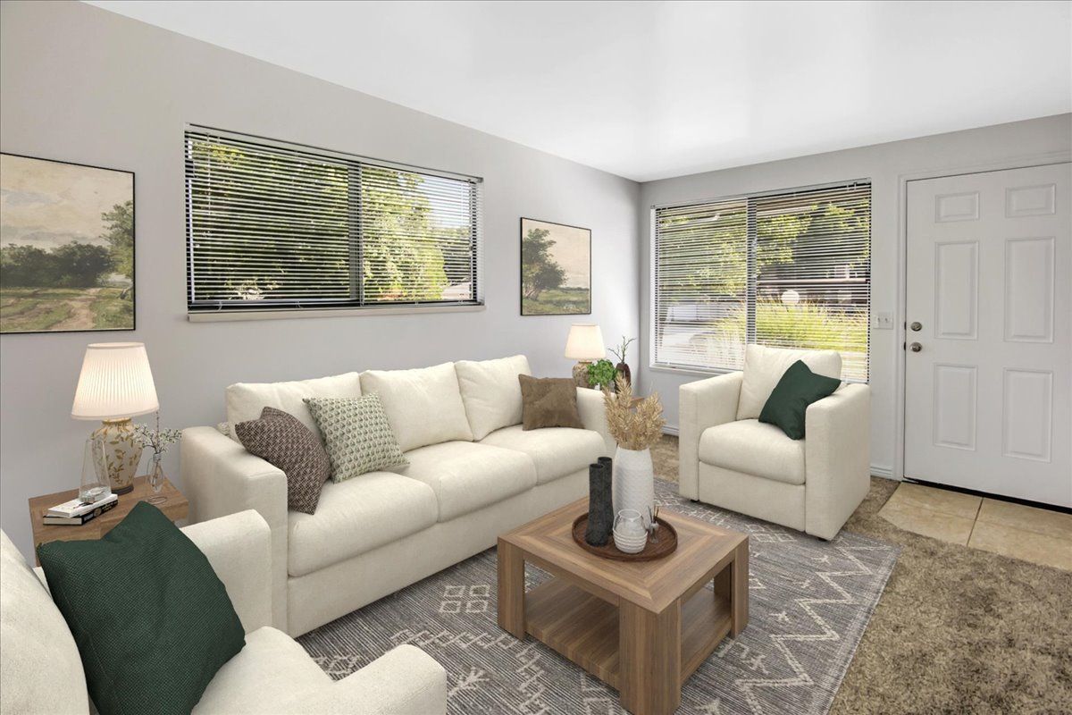 Living room with white sofa and armchairs, coffee table, rug, artwork, and windows.