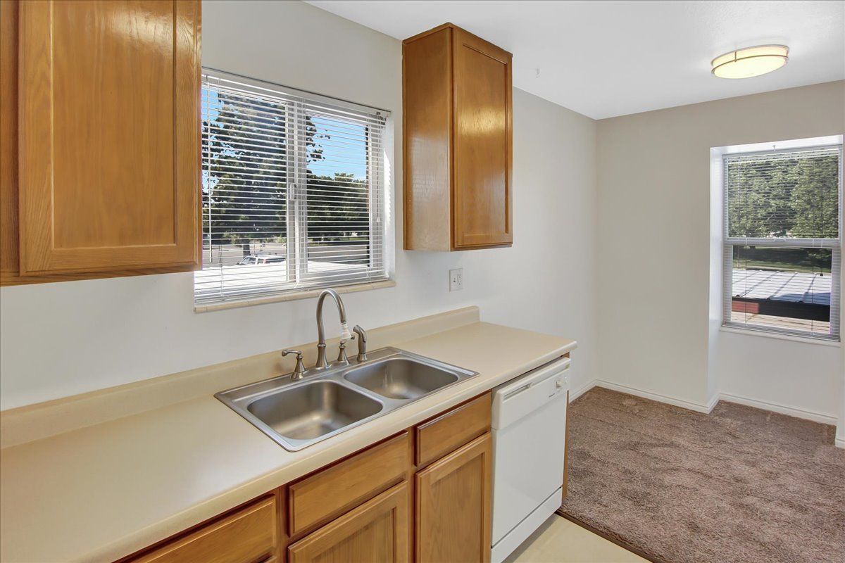 Kitchen with light-colored cabinets, a double sink, a window with blinds, and a dishwasher.