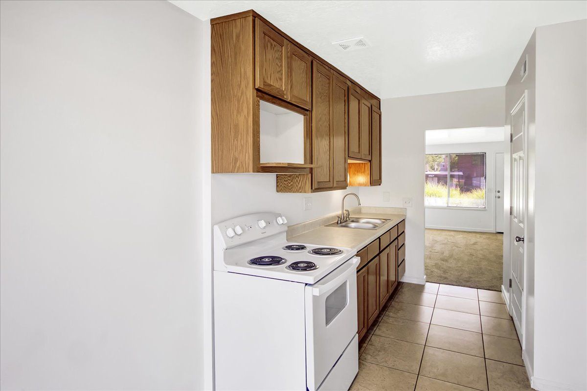 Small kitchen with white appliances, wooden cabinets, and beige tile floor.