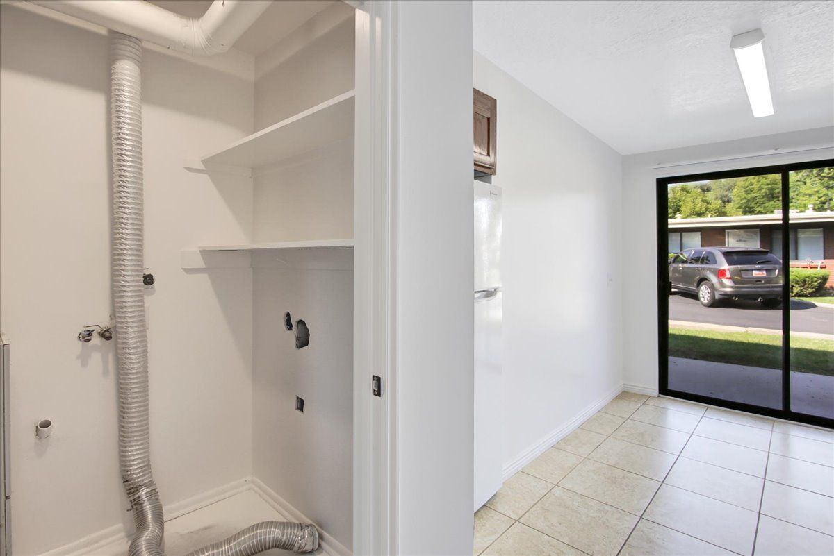 Laundry room with vent, shelves, and adjacent room with sliding doors and parked car.