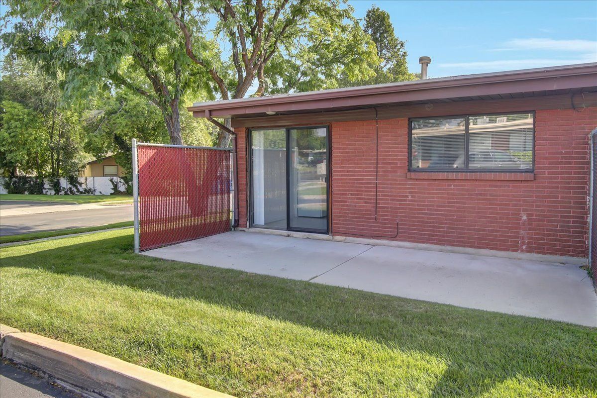 Red brick building with patio and sliding glass door, enclosed by a red chain link fence and green grass.