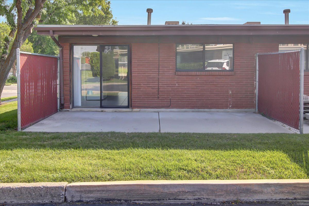 A brick building with a concrete patio enclosed by red chain-link fencing, green grass in front.