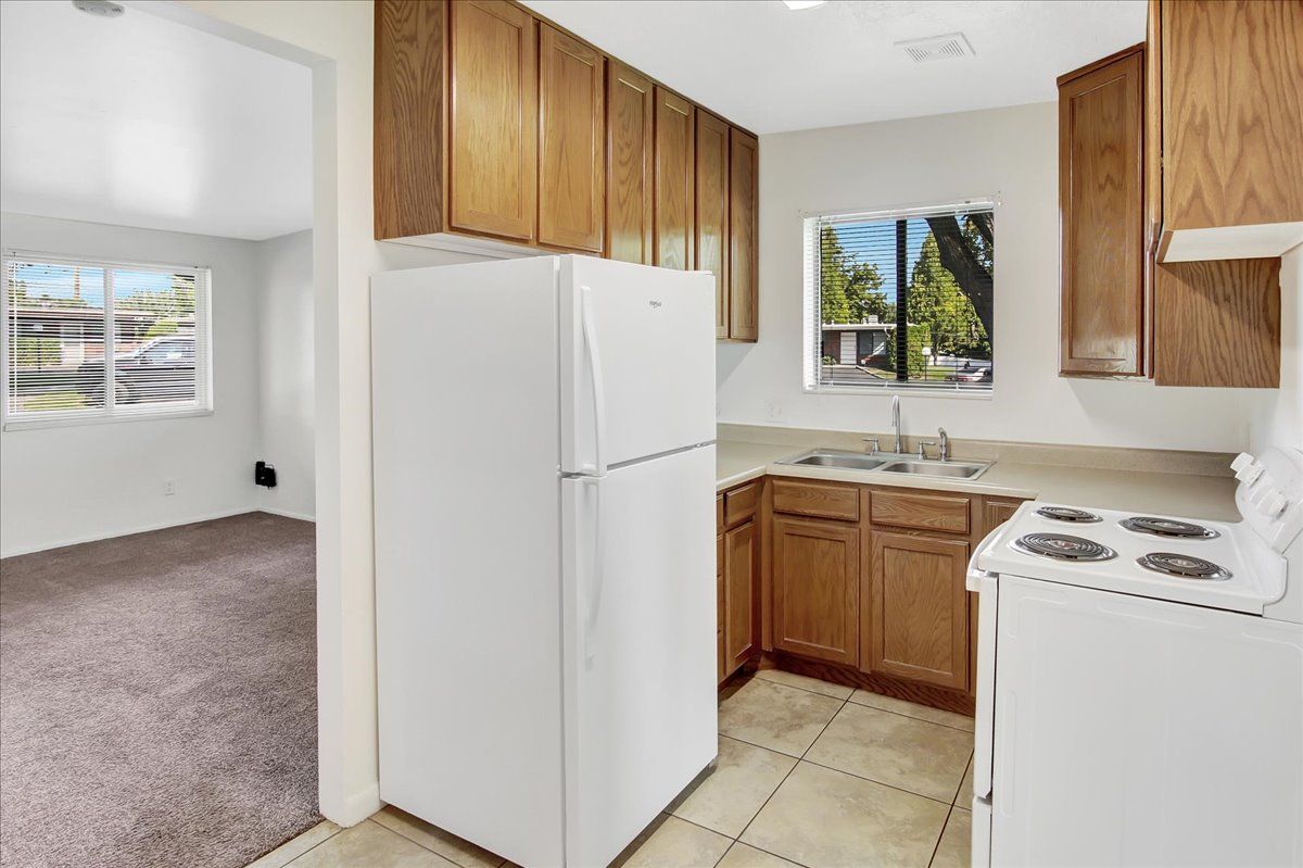 Kitchen with light brown cabinets, white refrigerator and stove, and view into a carpeted room.