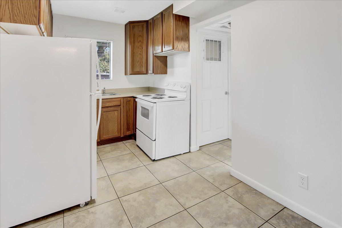 Kitchen with white appliances, brown cabinets, tile floor, and a doorway.