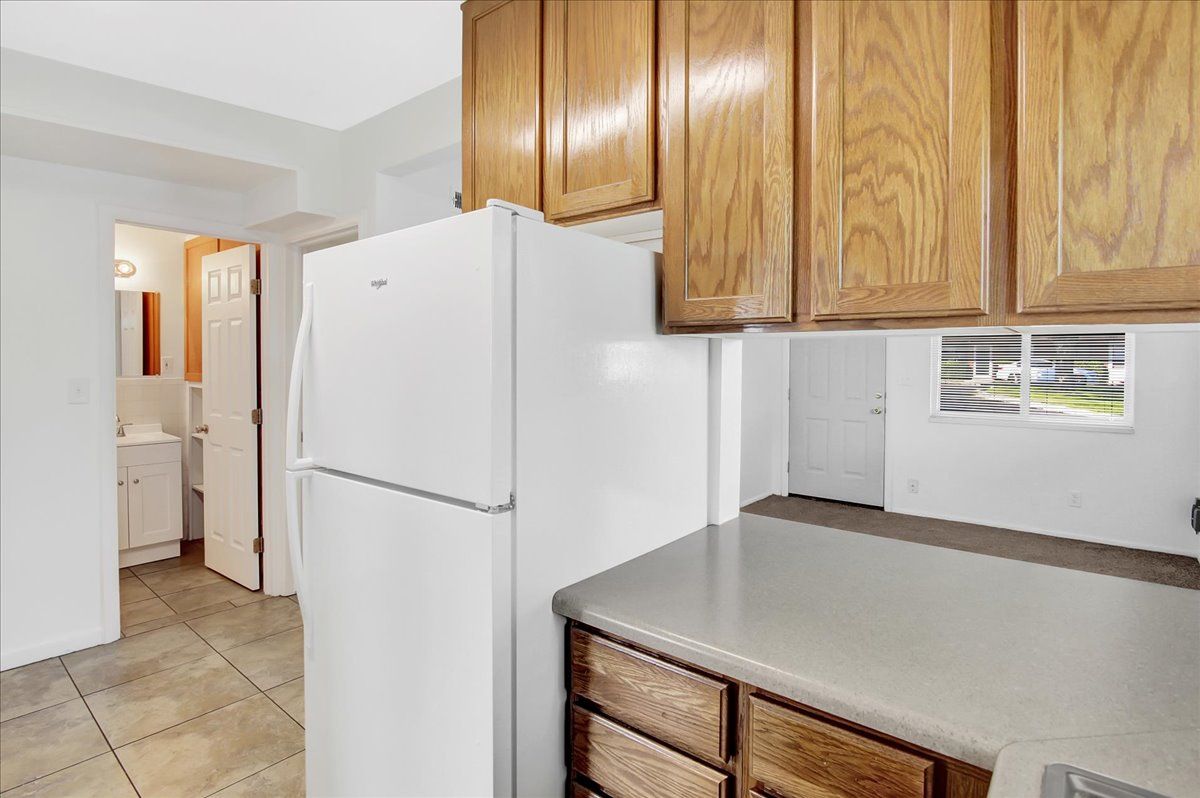Kitchen with wooden cabinets, white refrigerator, and view of a bathroom and a room with a window.