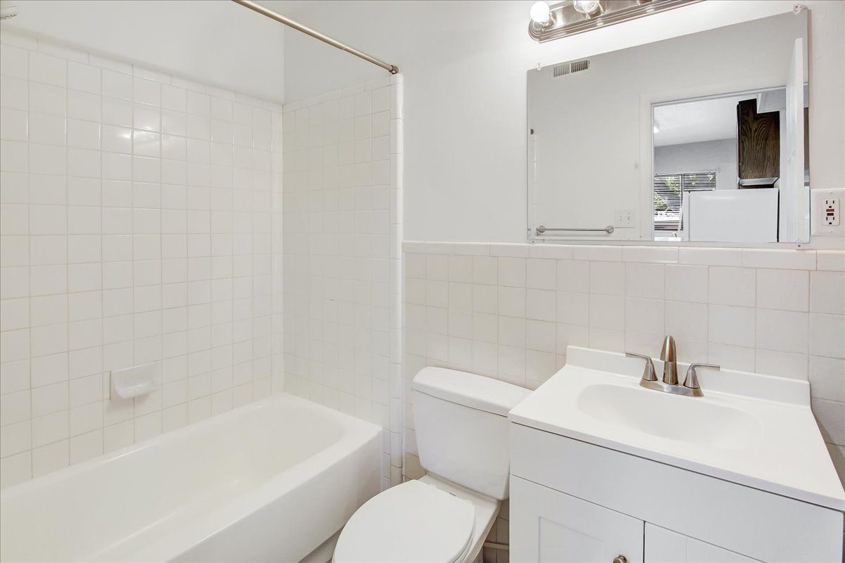 White bathroom with bathtub, toilet, sink, and mirror. White tiled walls.