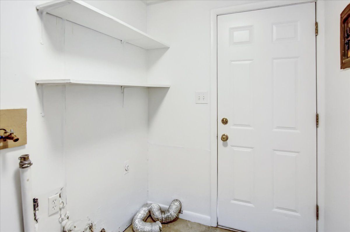 White laundry room with shelves, door, and dryer vent hose.