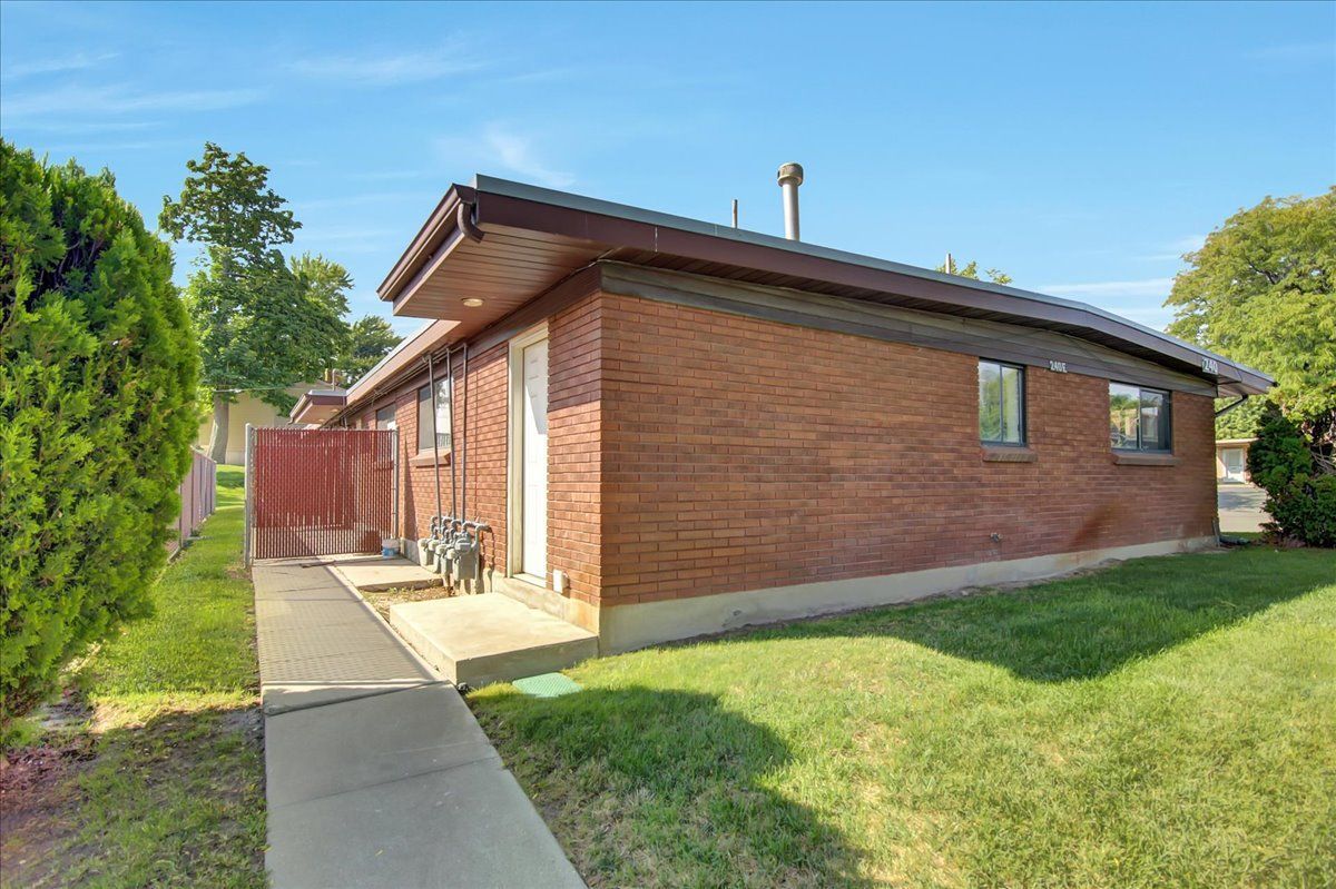 Brick building with a concrete walkway and a grassy yard under a blue sky.