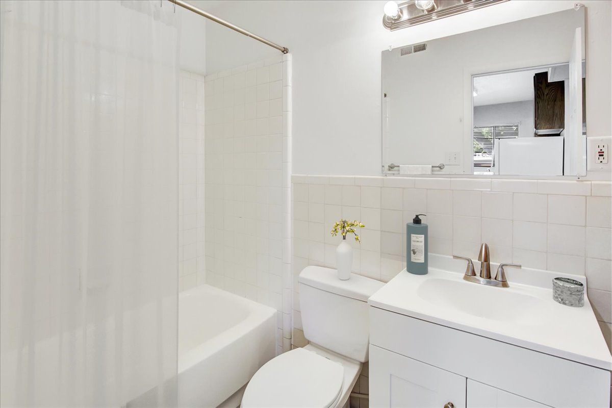 White bathroom with bathtub, toilet, sink, mirror, and toiletries.
