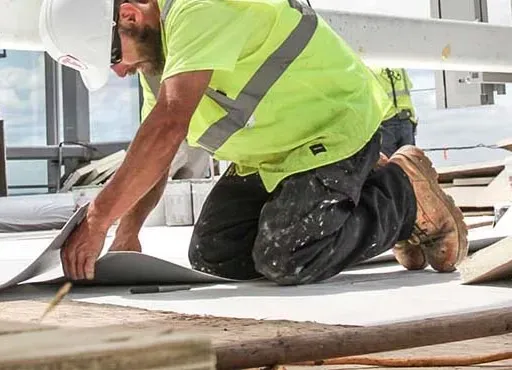 A construction worker is kneeling down while working on a roof.
