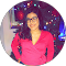 A woman in a pink shirt and glasses is standing in front of a christmas tree.
