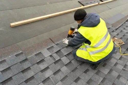 A man in a yellow vest is working on a roof.
